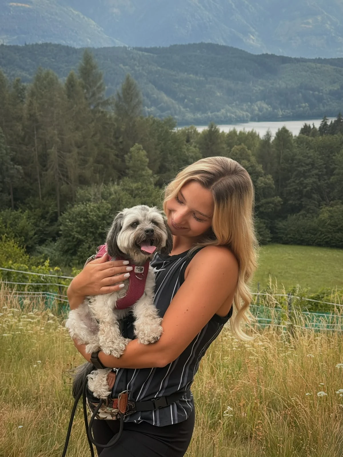Selina hält ihre Hündin Malia im Arm, im Hintergrund Berge und ein See